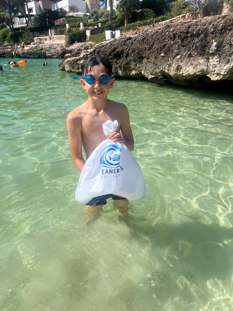 Ethan holding a Cleaner Seas Collective bag while collecting marine litter from the sea at a cove near Cala d’Or in Mallorca.