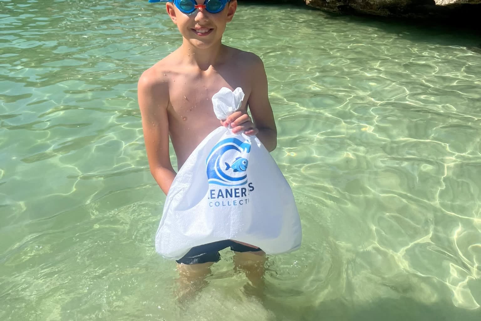 Ethan holding a Cleaner Seas Collective bag while collecting marine litter from the sea at a cove near Cala d’Or in Mallorca.
